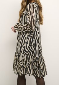 Vestido de estampado de cebra en beige y negro, con mangas largas, un dobladillo con volantes y una silueta fluida de textura ligera.