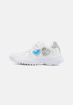 Weißer Kindersneaker mit klobiger Sohle, blauen und silbernen glitzernden Herzapplikationen und Klettverschluss vor einfarbigem Hintergrund.
