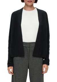 Dunkelblauer, gestrickter Cardigan mit offenem Vorderteil, gerippter Textur und langen Ärmeln, getragen über einem weißen Hemd und grauen Hose.