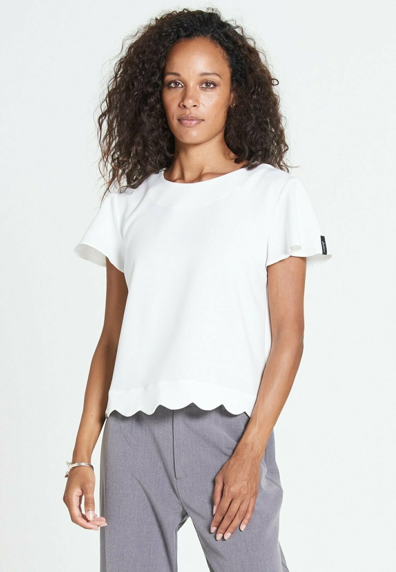 Top bianco a maniche corte con orlo scallop, realizzato in tessuto morbido. Abbinato a pantaloni grigi chiari su misura, che mostrano un design semplice e moderno.