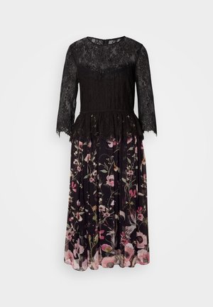 Robe en dentelle noire avec des manches trois-quarts, taille peplum, et jupe à motif floral dans des tons de rose et de vert sur un fond noir.