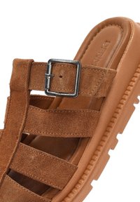 Sandalo in suede marrone con quattro cinturini orizzontali, un accento a fibbia e una suola in gomma testurizzata, con una fodera interna liscia.
