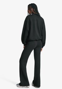Sort sweatshirt og flagrende sorte bukser, begge lavet af blødt materiale. Outfittet har en løs pasform og rund halsudskæring.