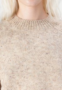 Beige gestrickter Pullover mit geripptem Ausschnitt, gesprenkelter Textur und lockerer Passform, hergestellt aus einem weichen Wollmix.