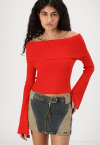 Top rosso a coste con spalle scoperte e lunghe maniche a campana, abbinato a una mini gonna di jeans con zip e dettagli in patchwork.