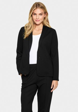 Schwarzer Blazer aus glattem Stoff, mit einem einzelnen Knopfverschluss, Reverskragen und zwei vorderen Taschen, kombiniert mit einem weißen Oberteil.