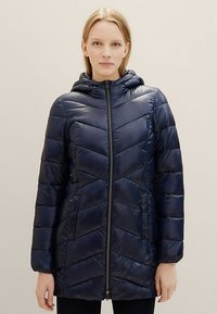 Tamsiai mėlyna pūkinė striukė su ševrono raštu, gobtuvu, ilgomis rankovėmis ir priekinio užtrauktuko uždarymu; turi šonines kišenes ir lygų paviršių.