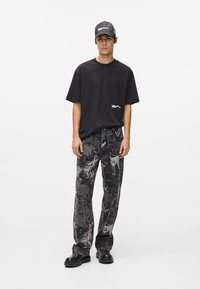 Μαύρο κοντομάνικο μπλουζάκι με λογότυπο, συνδυασμένο με χαλαρού τύπου τζιν σε μαύρο και γκρι σχέδιο. Η εμφάνιση ολοκληρώνεται με μαύρο καπέλο και χοντρές μαύρες παπούτσια.