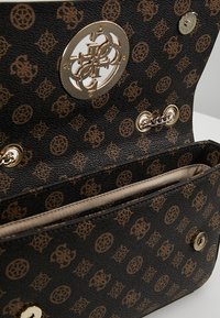 Sac à main en cuir noir avec motif marron en relief. Il possède une fermeture métallique, un détail en chaîne et une doublure intérieure beige avec un compartiment unique.
