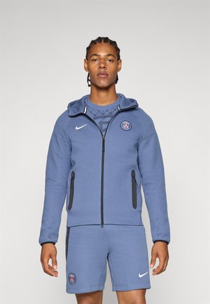 Blue hoodie with a zip front, black accents, and side pockets. Worn over a matching blue patterned shirt and shorts, featuring logos.