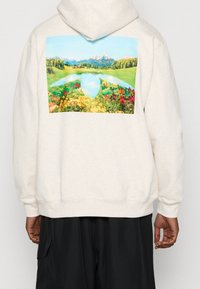 Cremiger Kapuzenpullover mit einem bunten Landschaftsdruck auf dem Rücken, der Berge, einen See und lebhafte Blumen zeigt. Gerippte Bündchen und Saum.