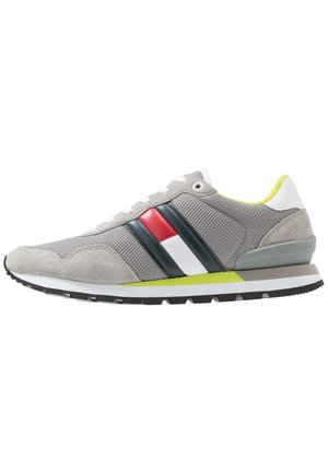 Grijze mesh en suède sneaker met witte zool, zwarte, rode en witte zijstrepen, neongele accenten en grijze hielondersteuning.