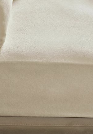 Nahaufnahme eines beigen Sofas mit strukturierter Stoffoberfläche und passendem Kissen auf der linken Seite.