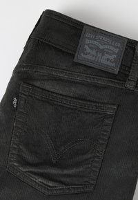 Jeans Levi's en velours côtelé noir montrant la poche arrière, la petite étiquette Levi's et le patch en cuir de la marque sur la ceinture.
