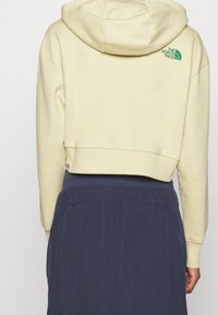 Felpa corta beige con logo verde "The North Face" sulla parte superiore della schiena abbinata a una gonna blu scura a vita alta con due tasche posteriori.