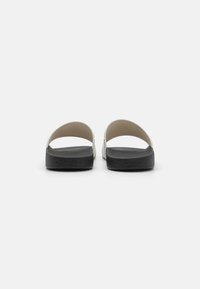 Sorte skum slide sandaler med en hvid rem, der har en glat overflade og minimalistisk design. Logo trykt på siden.