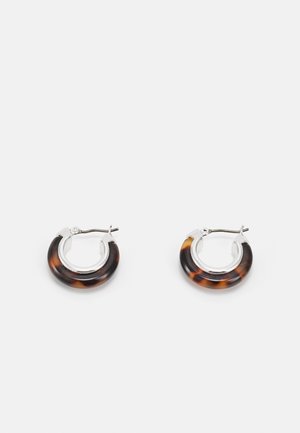 Petites boucles d'oreilles créoles avec dessus en argent et parties inférieures arrondies au motif écaille sur fond blanc.