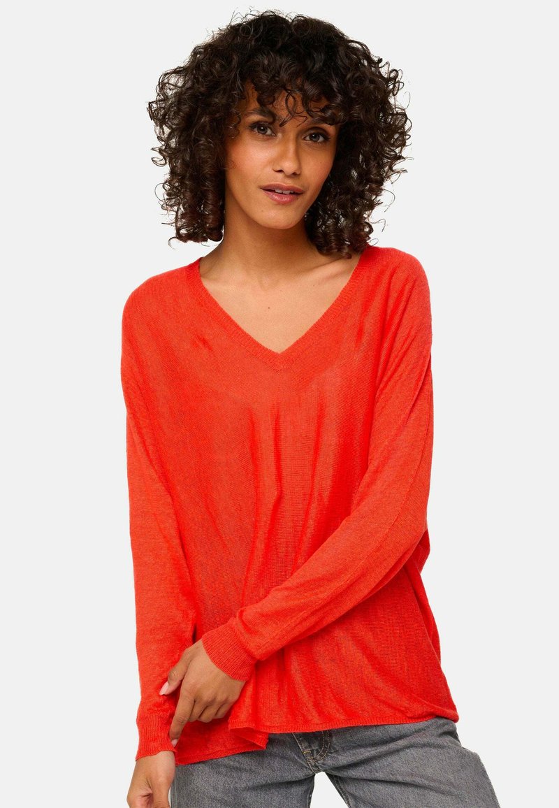 Roter, leichter V-Ausschnitt-Pullover mit langen Ärmeln, lässiger Passform und strukturiertem Finish. Kombiniert mit lässigen grauen Jeans.