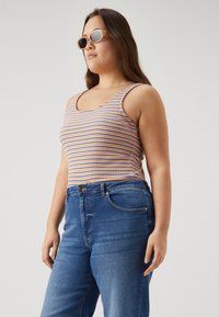 Top de alças riscado em azul, laranja e branco com decote quadrado, combinado com jeans de cintura alta azuis. Textura do tecido suave.