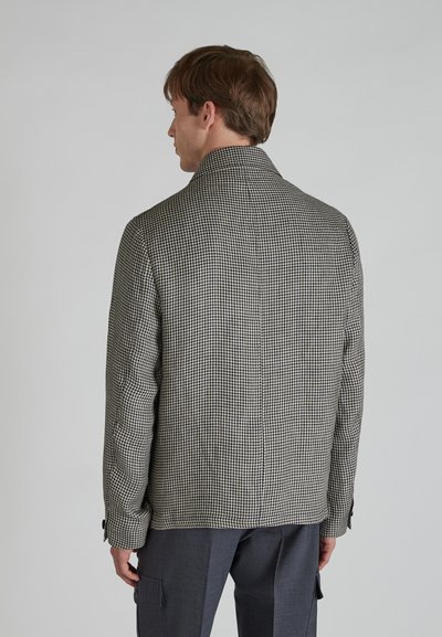 Czarna i biała marynarka w wzór houndstooth z kołnierzem, płaskimi klapami i zapięciem na guziki na mankietach, charakteryzująca się gładką fakturą i dopasowanym krojem.