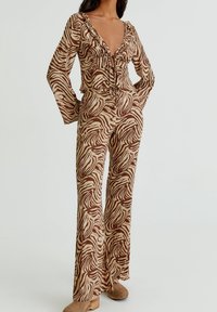 Femme portant un haut à manches longues en imprimé zèbre marron et beige et un pantalon large assorti avec des chaussures plateforme beiges.