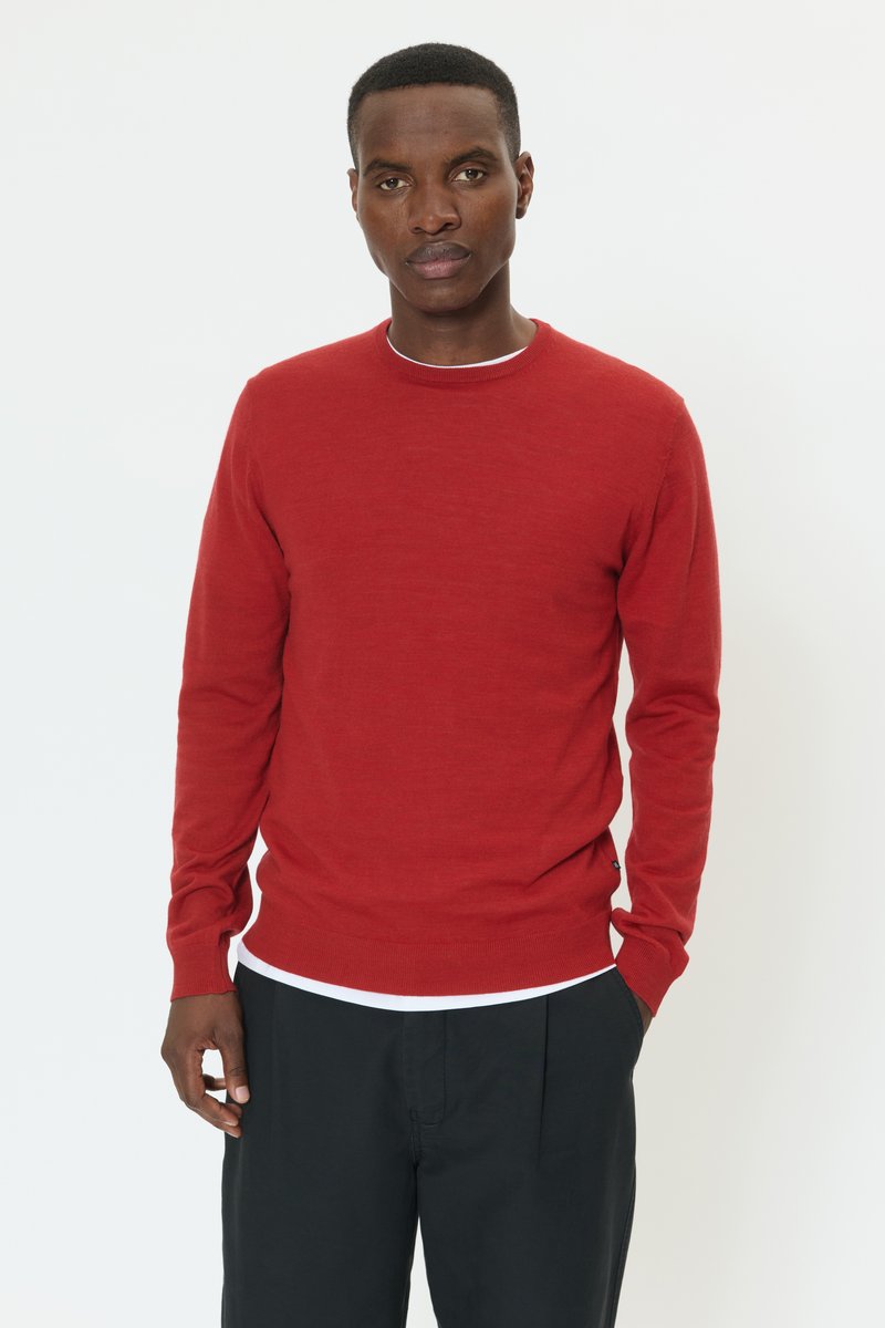 Pulover roșu tricotat, cu guler rotund și mâneci lungi. Purtați peste o cămașă albă, asortat cu pantaloni negri, având o textură subtilă.