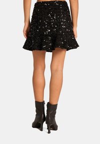 Zwarte flair minirok van sequined stof, met een gestructureerde afwerking. Gecombineerd met zwarte enkellaarsjes met hak.