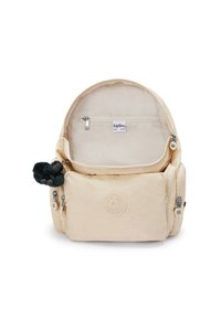 Zaino Kipling beige con il compartimento principale aperto, tasche frontali e laterali con cerniera, e un piccolo portachiavi a forma di scimmia nera attaccato.