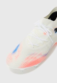 Weißer Fußballschuh mit mehrfarbigem Verlaufsmuster und blauen sowie rosa Akzenten. Strickobermaterial, Schnürverschluss und Kunststoffstollen an der Sohle.