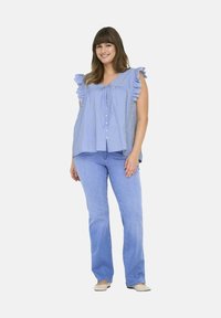 Blusa a righe blu chiaro con maniche a balze, caratterizzata da dettagli ricamati e una chiusura con bottoni. Abbinata a jeans blu chiaro e scarpe basse.