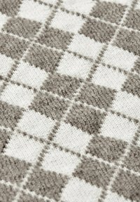 Tessuto testurizzato con un motivo a scacchiera in grigio e bianco. Il materiale appare morbido con diverse spessore di filato nelle sezioni quadrate.
