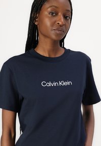 Marine bomull T-skjorte med korte ermer og rund hals, med kontrasterende hvit "Calvin Klein" logo på brystet. Glatt tekstur.