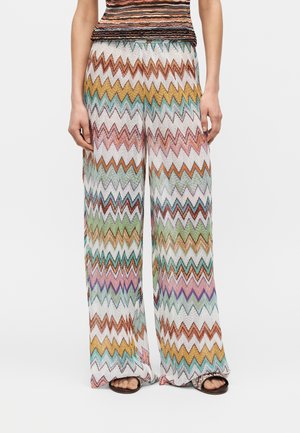 Laiade säärega püksid mitmevärvilise siksakmustriga oranži, rohelise, lilla ja valge toonides, mustade avatud varbaga sandaalidega.