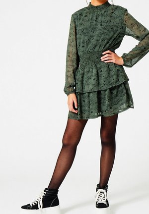 Robe verte à couches avec des manches longues, présentant une taille froncée et un motif céleste. Associée à des baskets montantes noires.