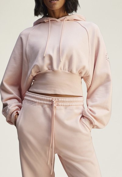 Pink cropped hoodie with drawstrings, ribbed texture at the waist, paired with matching sweatpants featuring an elastic waistband and pockets.