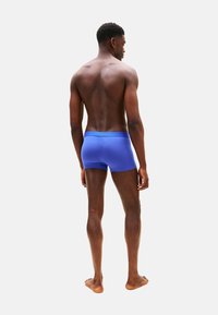 Calzoncillos bóxer de algodón azul, diseño ajustado, color sólido, textura suave, cintura baja con cinturilla en contraste. Modelo visto desde atrás.
