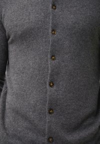Šedý vlněný cardigan s přiléhavým střihem, který má po celé délce nahoře šest hnědých knoflíků a měkký, strukturovaný povrch.