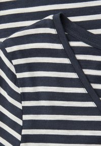 Tmavě modrá a bílá látka s vodorovnými pruhy a výstřihem do V, detailní záběr na texturu a vzor textilu.