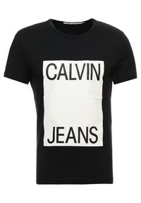 Zwarte katoenen T-shirt met een grote witte rechthoekige grafische print met zwarte tekst, waarop "CALVIN JEANS" staat, aan de voorkant. Standaard pasvorm.