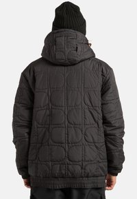 Czarna pikowana kurtka z kapturem, elastycznymi mankietami i dołem. Tył ozdobiony jest geometrycznym wzorem wypukłych owalnych kształtów.