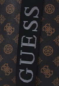 Czarna teksturowana torba z brązowym wzorem logo, z szerokim plecionym paskiem z białym napisem "GUESS".
