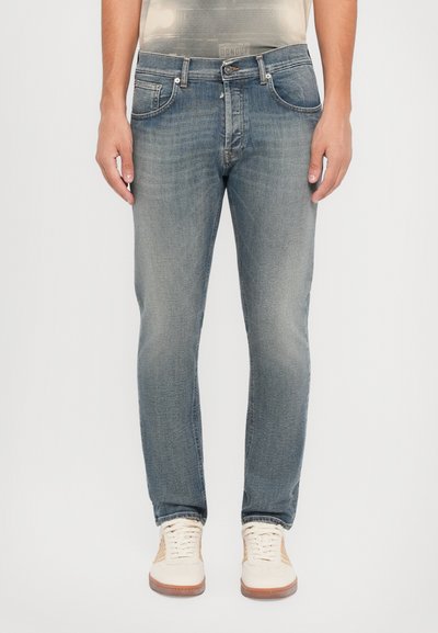 Verblasste blaue Denim-Jeans mit schlanker Passform, Fünf-Taschen-Design und dezenten Steppdetails, getragen mit cremefarbigen Sneakers.