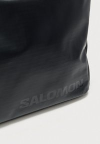 Μαύρο εκπαιδευτικό σακίδιο από ανθεκτικό υλικό, με κομψό σχεδιασμό, υφή επιφάνειας και ανάγλυφο λογότυπο "SALOMON".