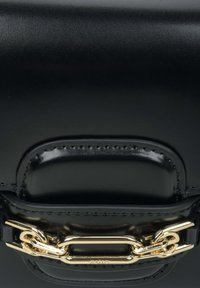 Czarna skórzana torebka o wyraźnym kształcie, gładkiej fakturze i złotym metalowym łańcuszku na przednim klapie.