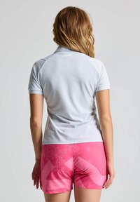 Helle graue Polo-Hemd mit kurzen Ärmeln und einer glatten Textur, kombiniert mit rosa gemusterten Shorts mit abstrakten Designs und kontrastierenden Farben.