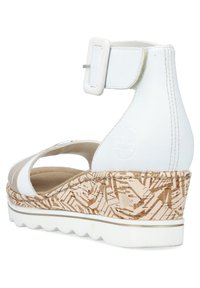 Sandales compensées blanches avec une bride de cheville réglable, semelle intermédiaire texturée en liège et semelle extérieure blanche flexible. Conception ouverte pour la respirabilité.