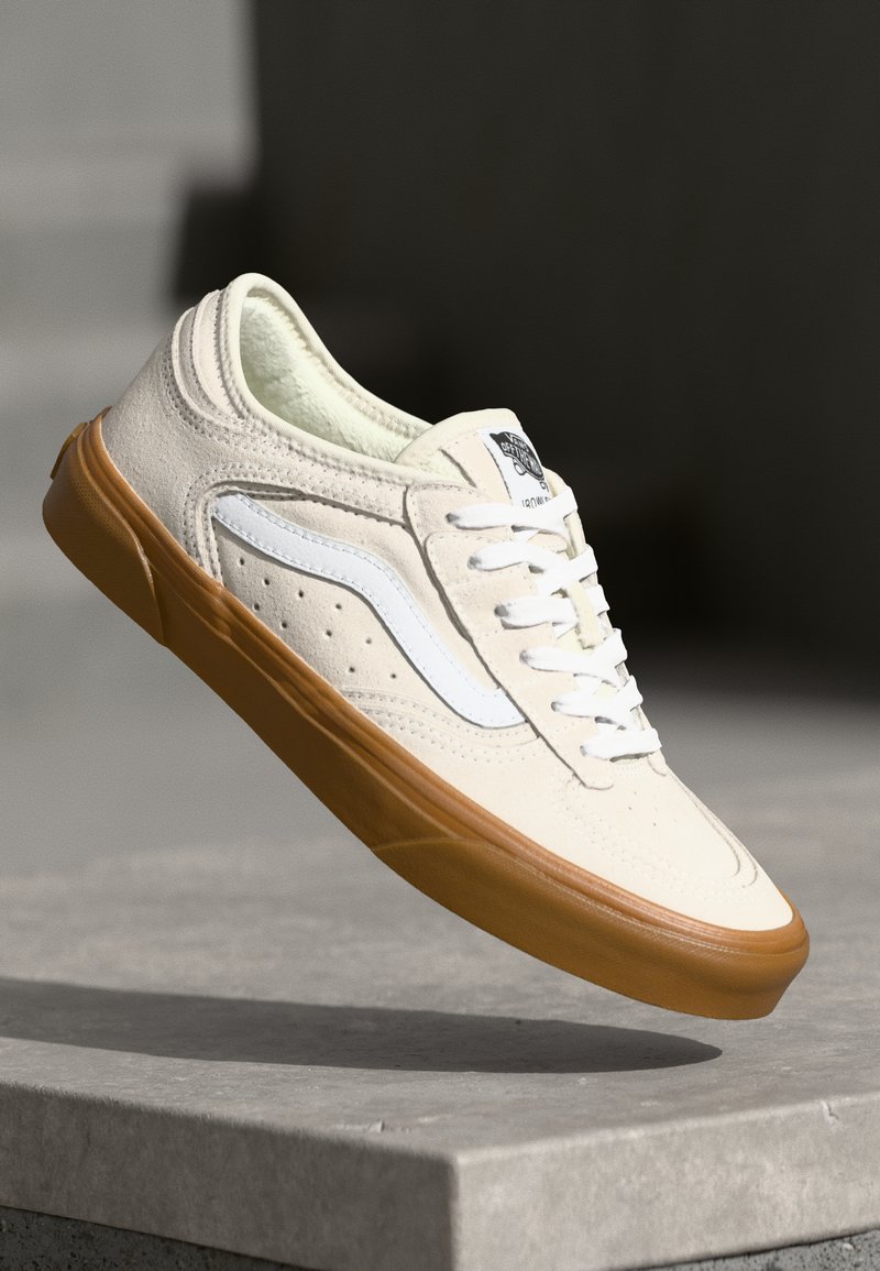 Beige semskede sneakers med hvite detaljer, som har et perforert design og en såle av gummigummi. Snørret med hvite skolisser.