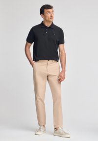 Svart polotröja med en liten logotyp, beige chinos och ljusa sneakers. Polotröjan har korta ärmar och en klassisk krage. Slät tygstruktur.
