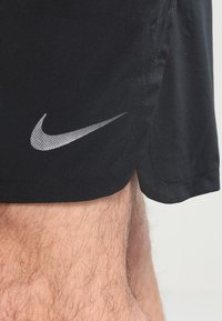 Schwarze Sportshorts mit glatter Textur, die ein reflektierendes Nike-Logo am Saum aufweisen. Das Design beinhaltet einen seitlichen Schlitz für Beweglichkeit.