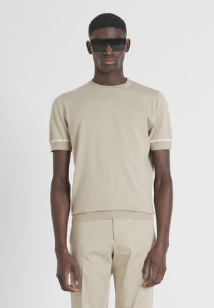 Beige trui met korte mouwen en een ronde halslijn, met een gestructureerd breisel en witte accenten op de mouwen. Gepaarde met beige op maat gemaakte broek.